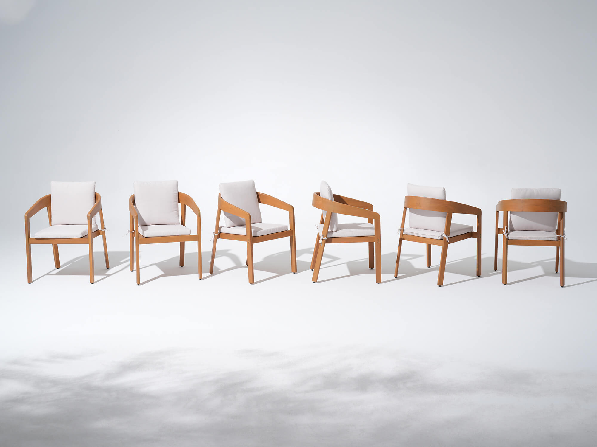 Six wucalyptus wooden dining chairs with white cushions arranged in a row - Sunsitt’s Modern Premium Outdoor Furniture
